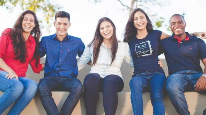 Fünf junge Menschen sitzen lachend auf einer Mauer