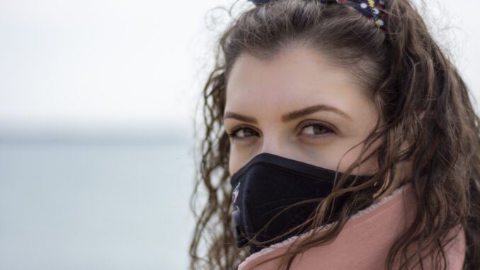 Eine junge Frau mit Gesichtsmaske vor dem Meer