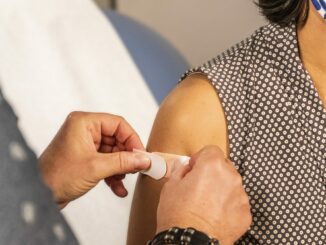 Ein Arzt klebt ein Pflaster auf die Impf-Einstichstelle