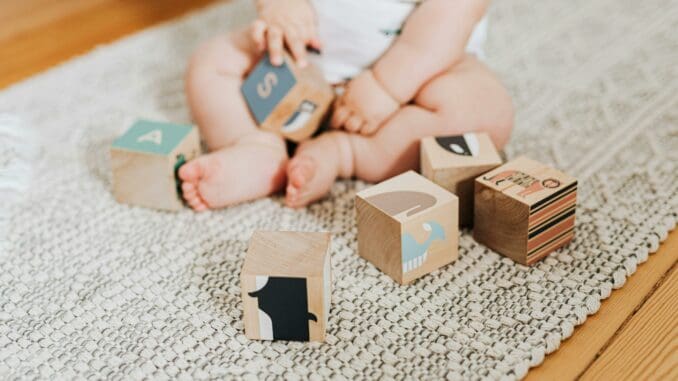 Zu sehen ist ein Baby, das mit hölzernen Alphabetblöcken spielt.