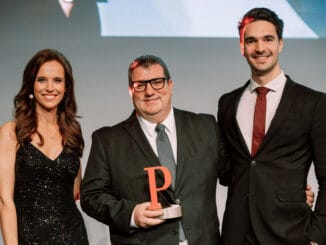 Zu sehen sind eine Moderatorin, Jürgen H. Gangoly (Mitte) und Philipp Grüll (rechts) bei der Verleihung in Berlin.