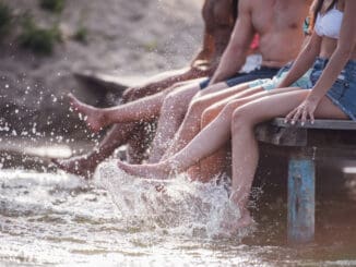 Cropped image of happy friends splashing water while sitting on pier at the sea
