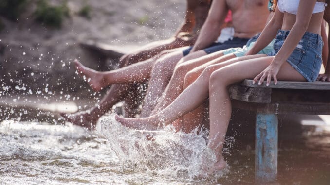 Cropped image of happy friends splashing water while sitting on pier at the sea